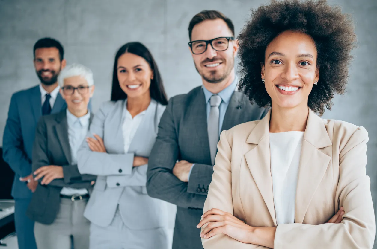 Five professionally dressed people in an office smiling at the camera
