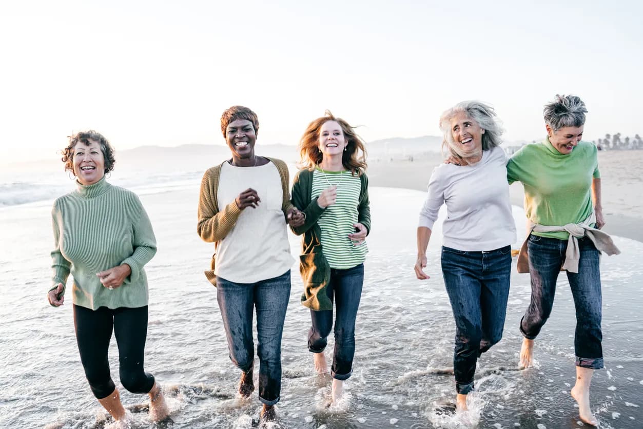 Five older women walking in the water on a beach