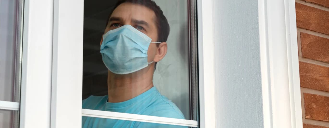 Person wearing a mask looking out a window