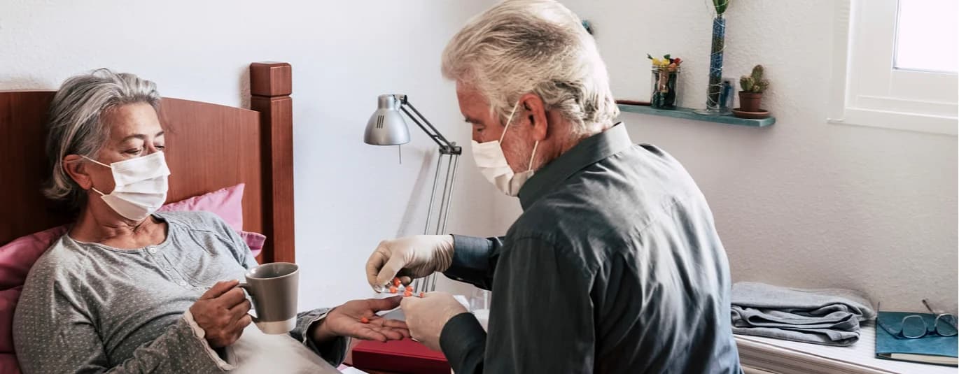 Man wearing a mask caring for a sick person with a mask in a bed