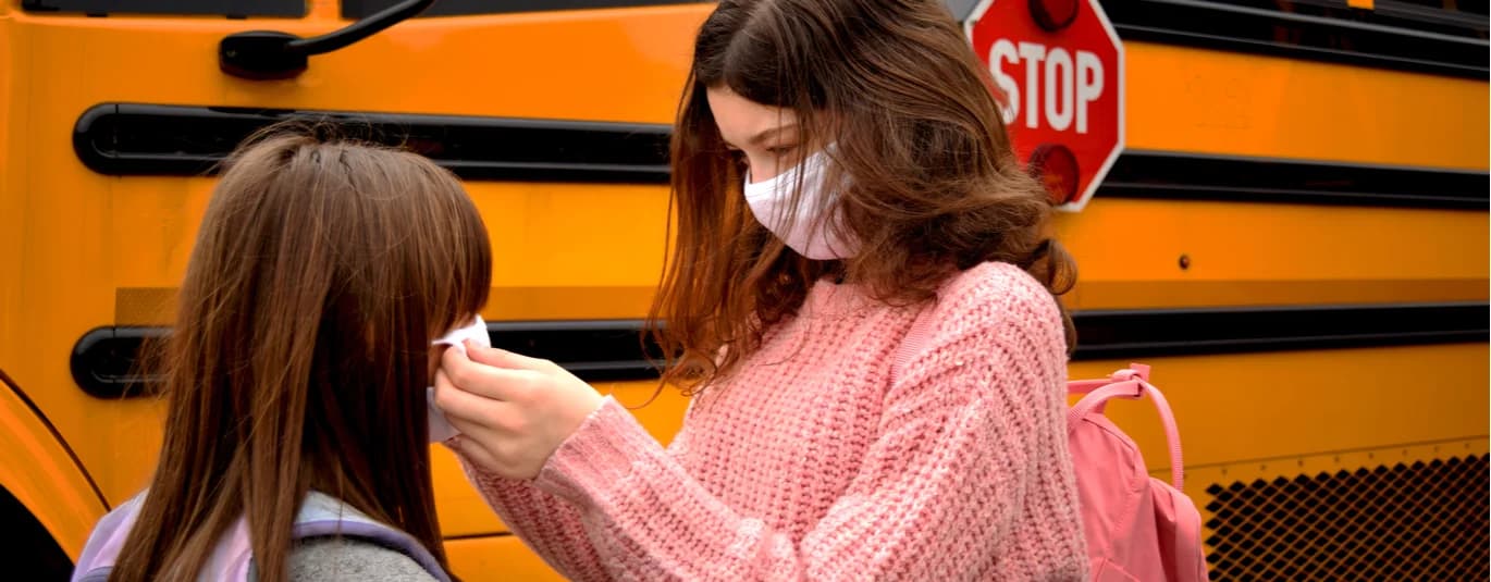 People wearing masks in front of a school bus