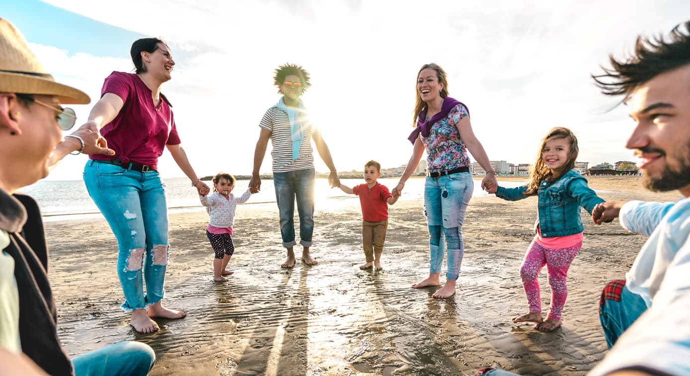 View point of young families dancing at beach on ring around the rosy style - Lifestyle joy concept with mixed race people having fun moment holding hands
