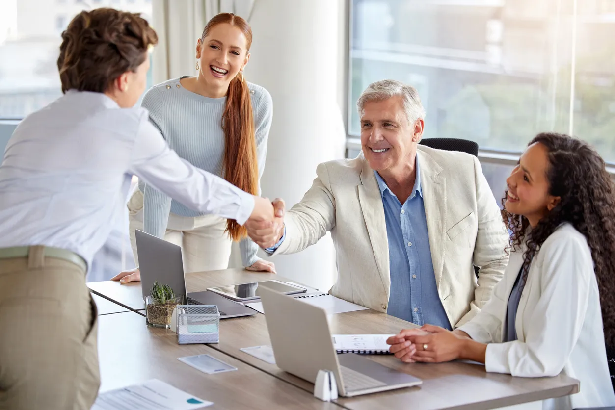 Four people at a meeting with laptops shaking hands