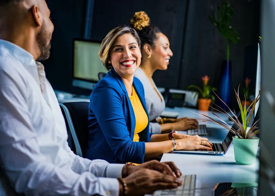 Three coworkers with laptops sitting together at a long table