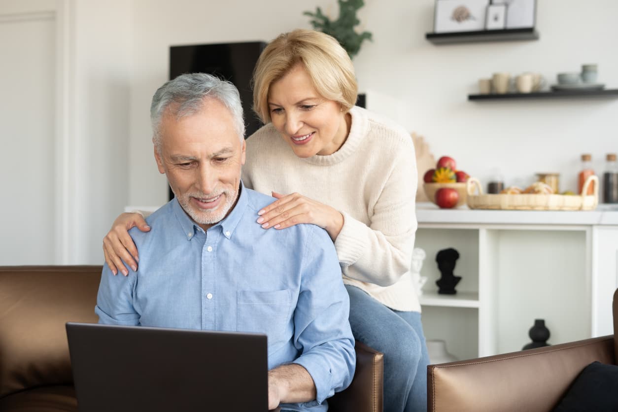 A male and female middle aged smiling couple looking at the computer
