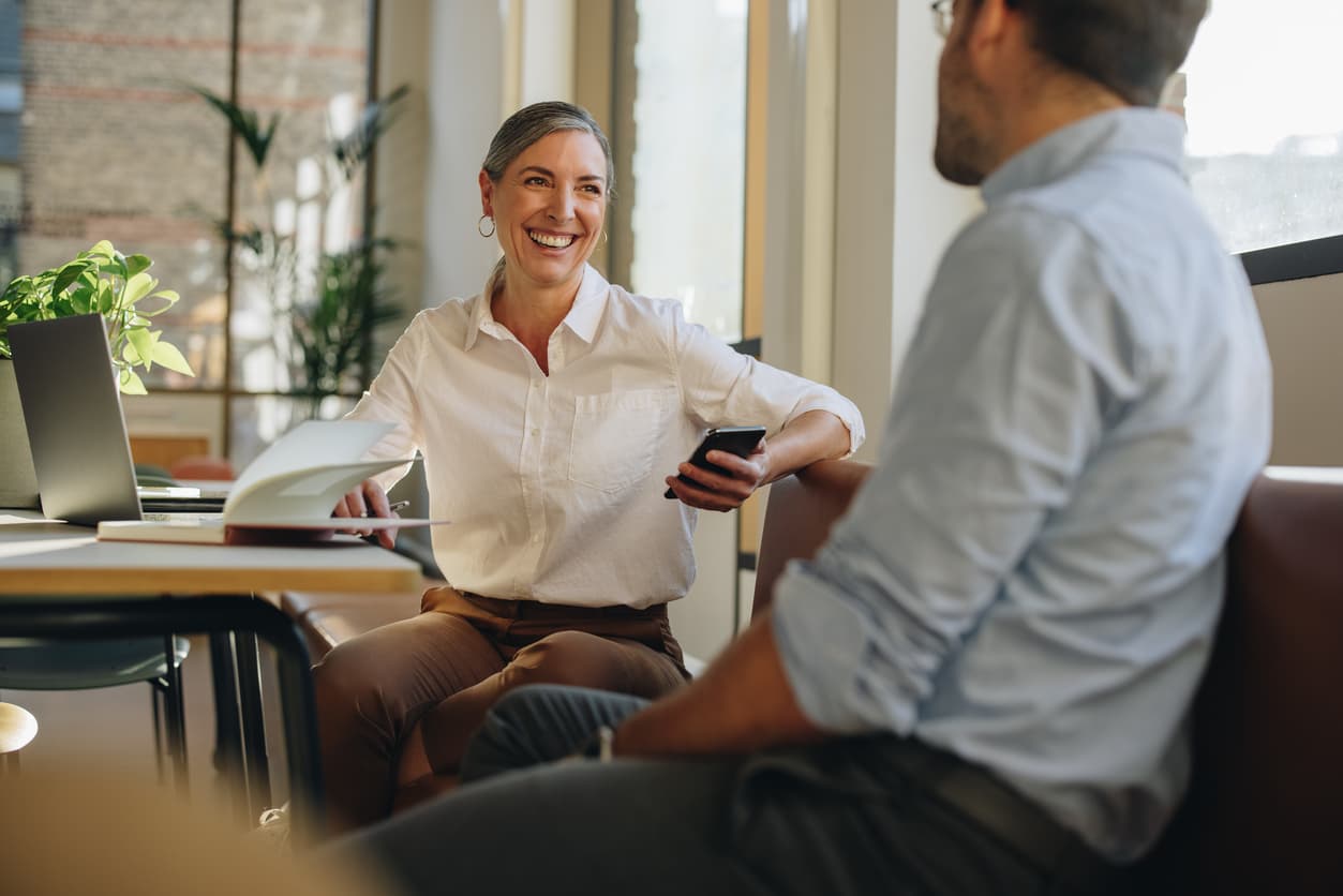 Businesswoman sitting at desk and explaining new project to coworker in an office.