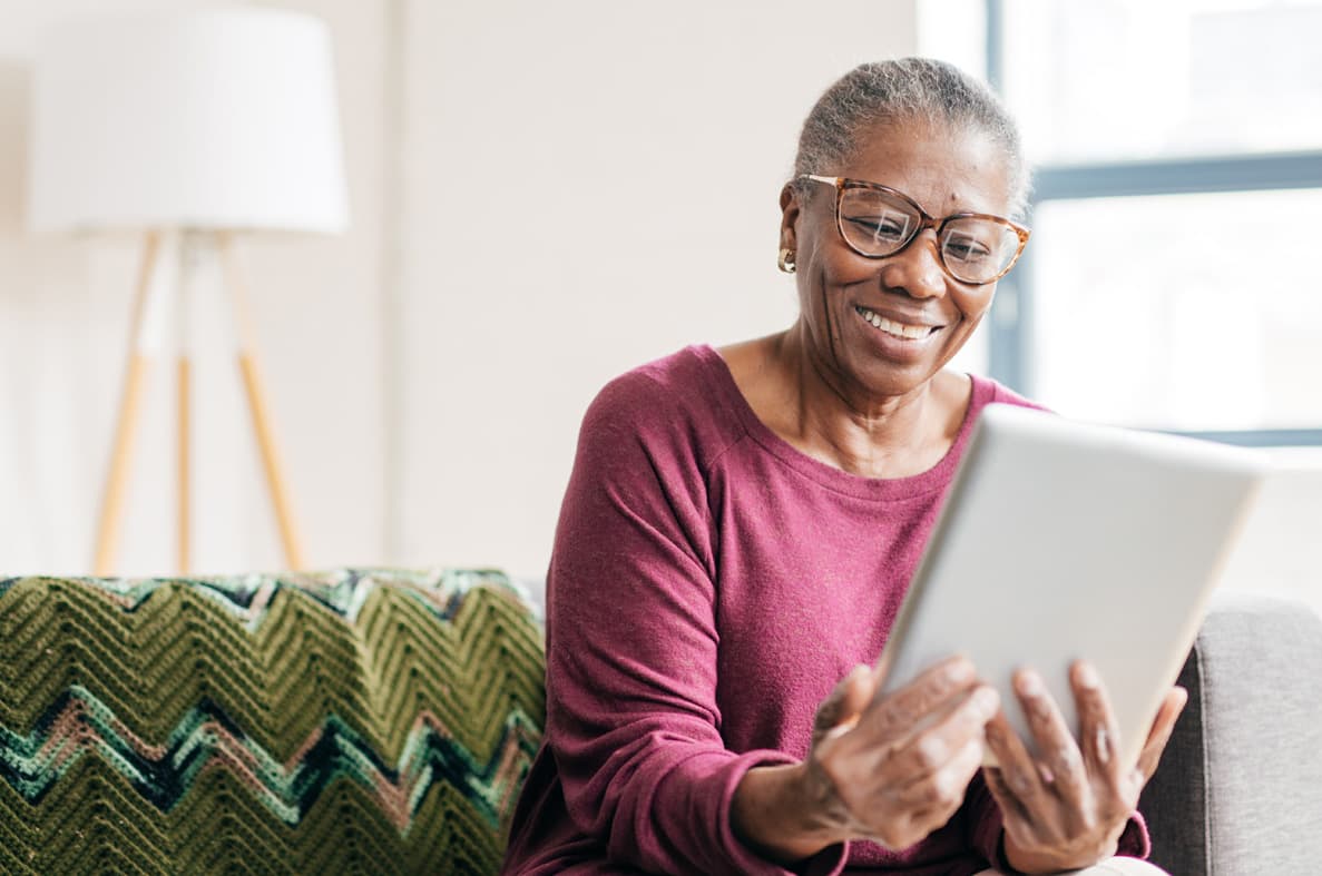 Old woman smiling while looking at her tablet